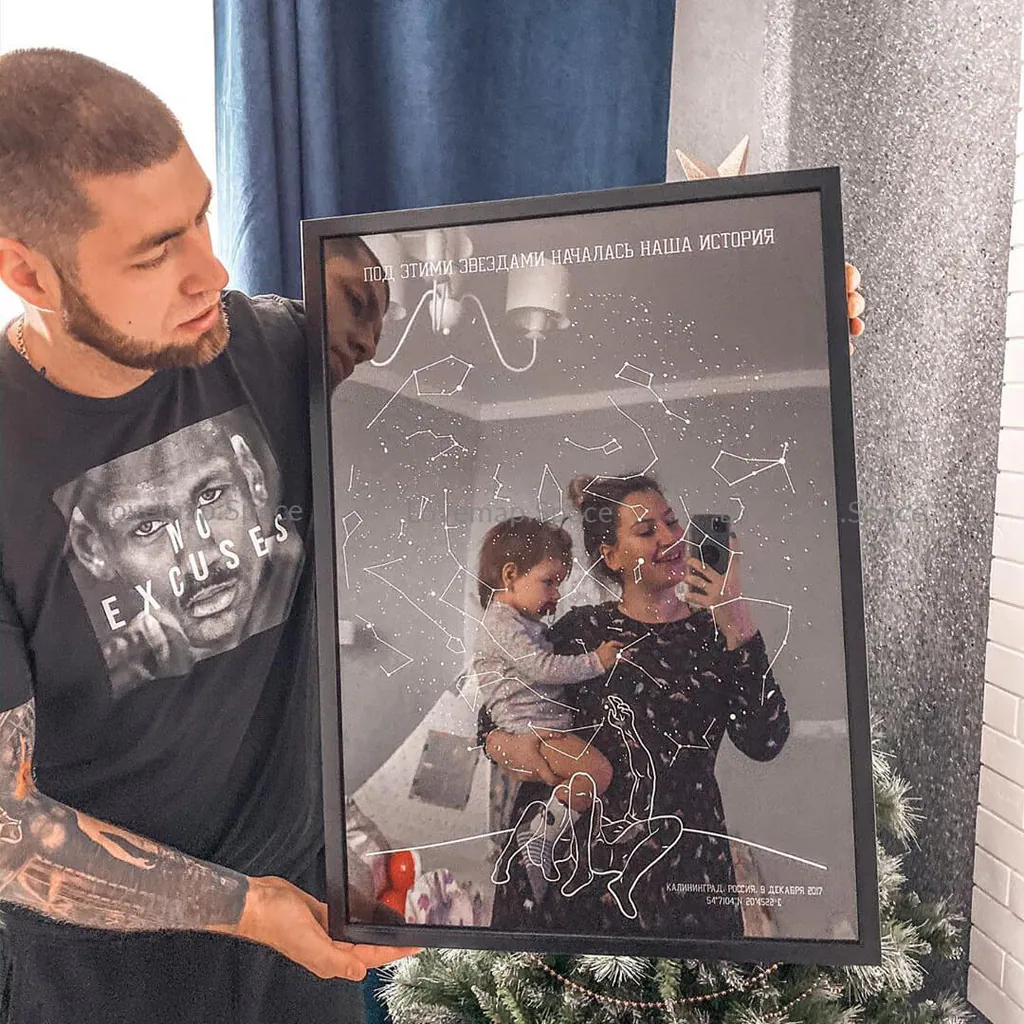 Мужчина держит звёздную карту с семейной фотографией в чёрной раме у новогодней ёлки
